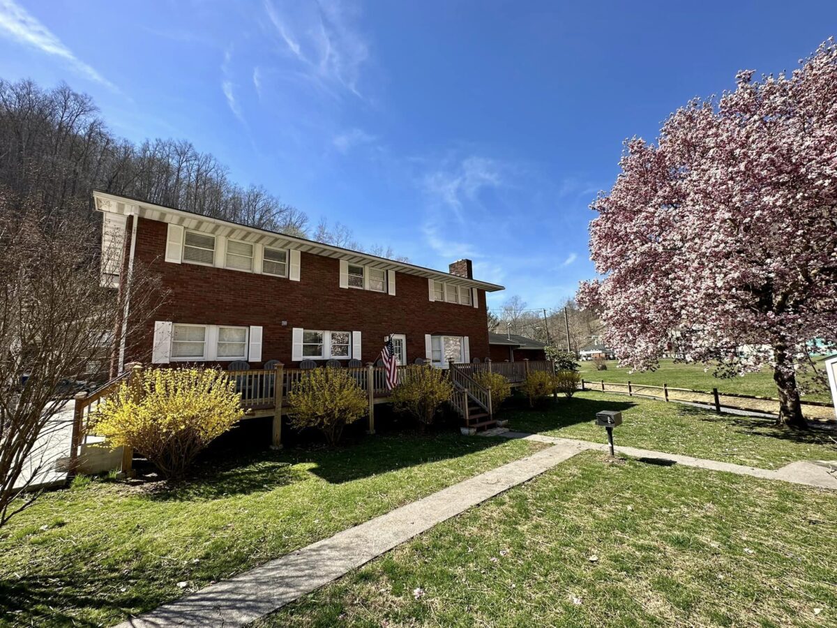 A brick home with trees and flowers in the front yard, providing Hatfield McCoy Trails Lodging.