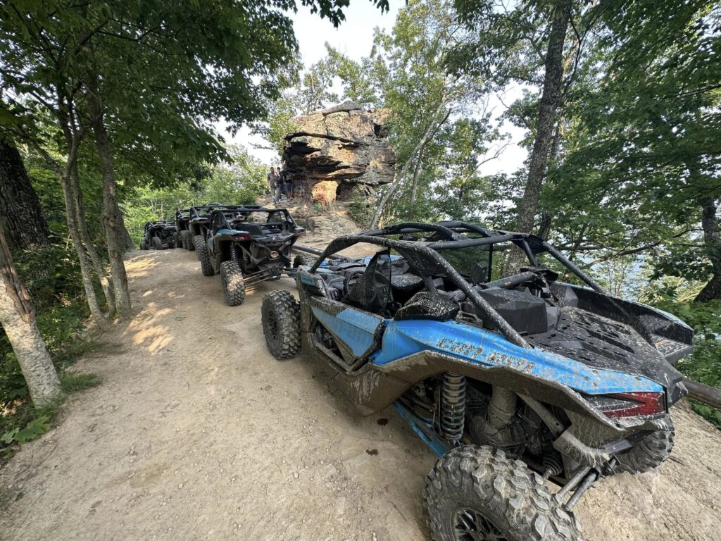 A group of blue ATVs from Hatfield McCoy SXS Rentals on a trail in the woods.