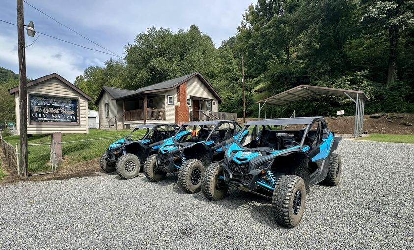 All-terrain vehicles parked in front of a cabin near a forested area, close to Hatfield McCoy Trails lodging.