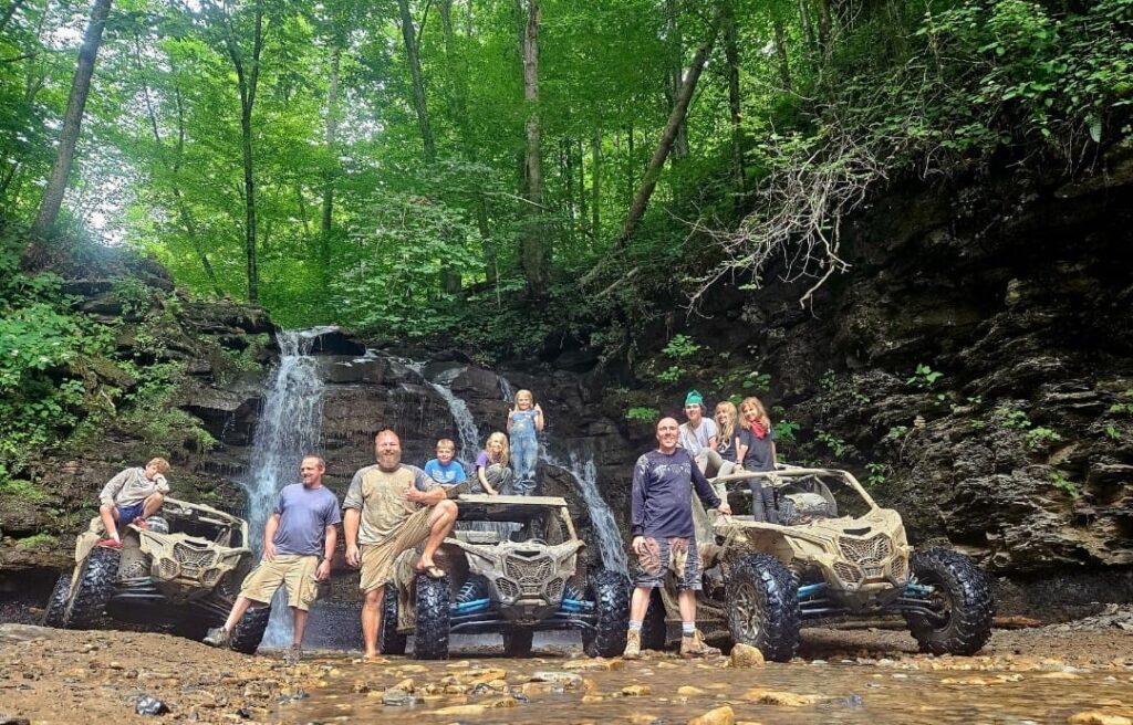 A group of people from Hatfield McCoy SXS Rentals posing in front of a waterfall in the woods.