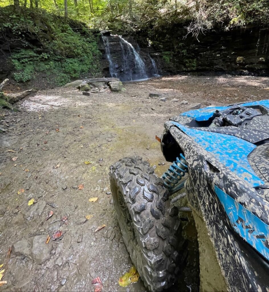 A blue Hatfield McCoy ATV is parked in front of a waterfall.