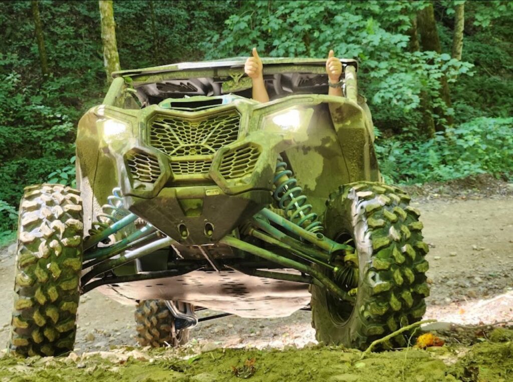 The Hatfield McCoy can-am maverick xp 1000 is driving through the woods.