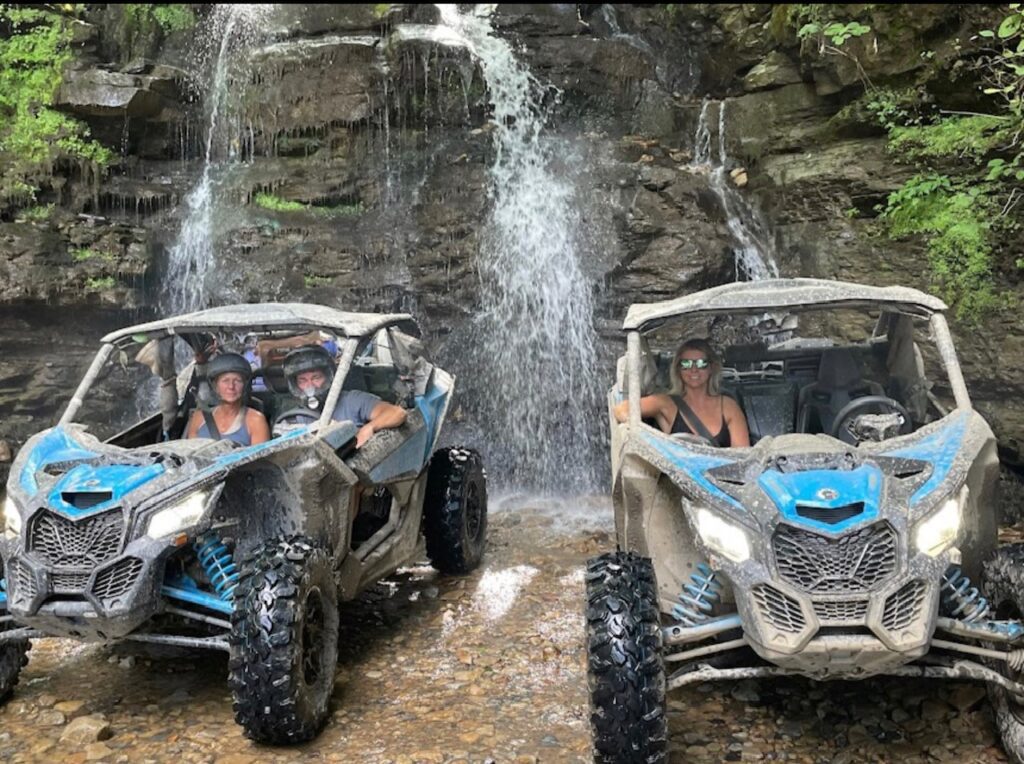 Two people on a Hatfield McCoy SXS Rentals can-am maverick utv in front of a waterfall.